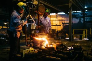 Molten metal is poured into a mold as foundry workers cast commercial parts and industrial components. 