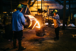 two men casting large metal components for farm equipment production